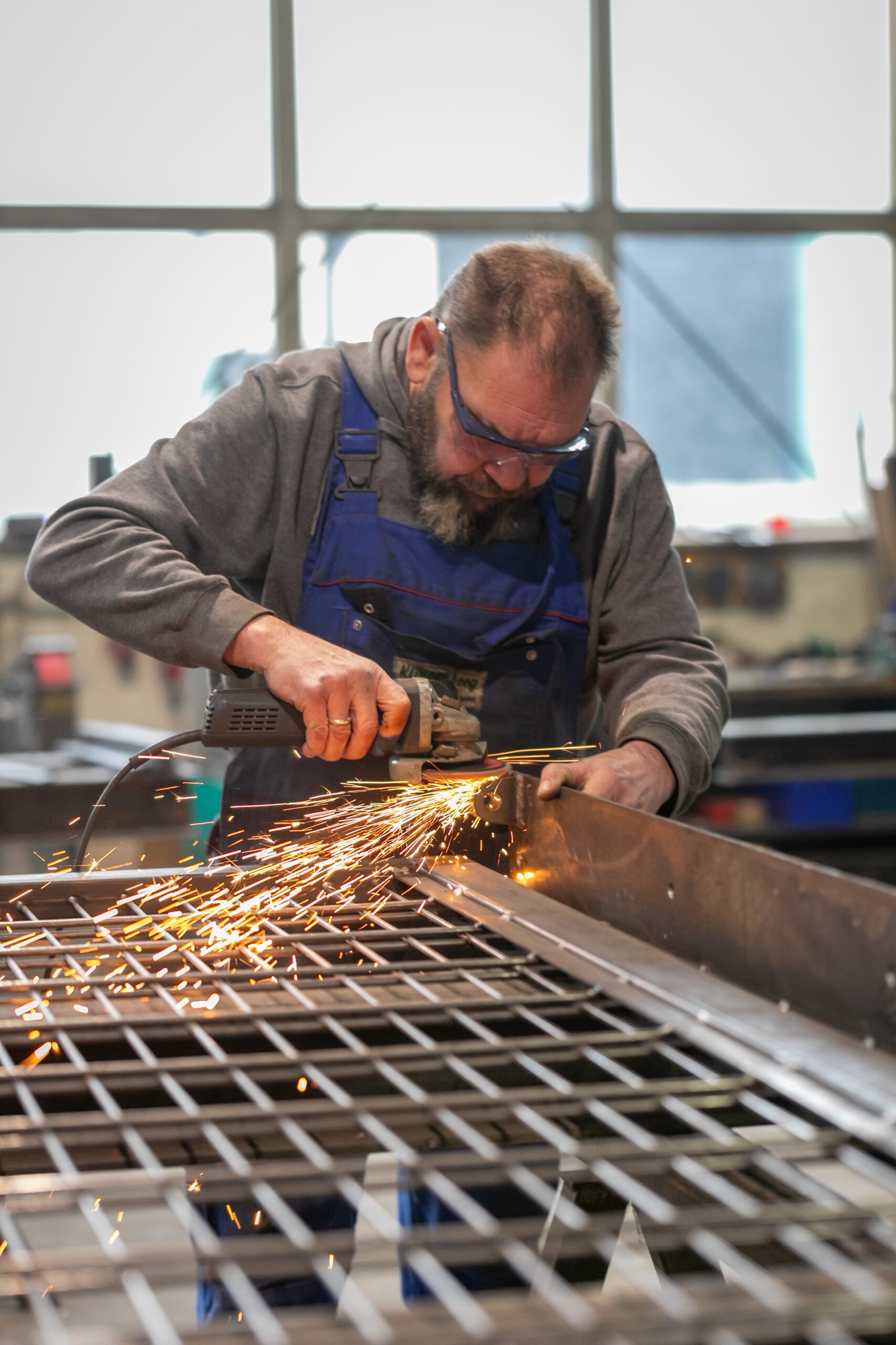 Mitarbeiter von Klingenberg Zaeune schleift Metallgitter, Funkenflug zeigt praezise Handwerk fuer langlebige Zaunanlagen.